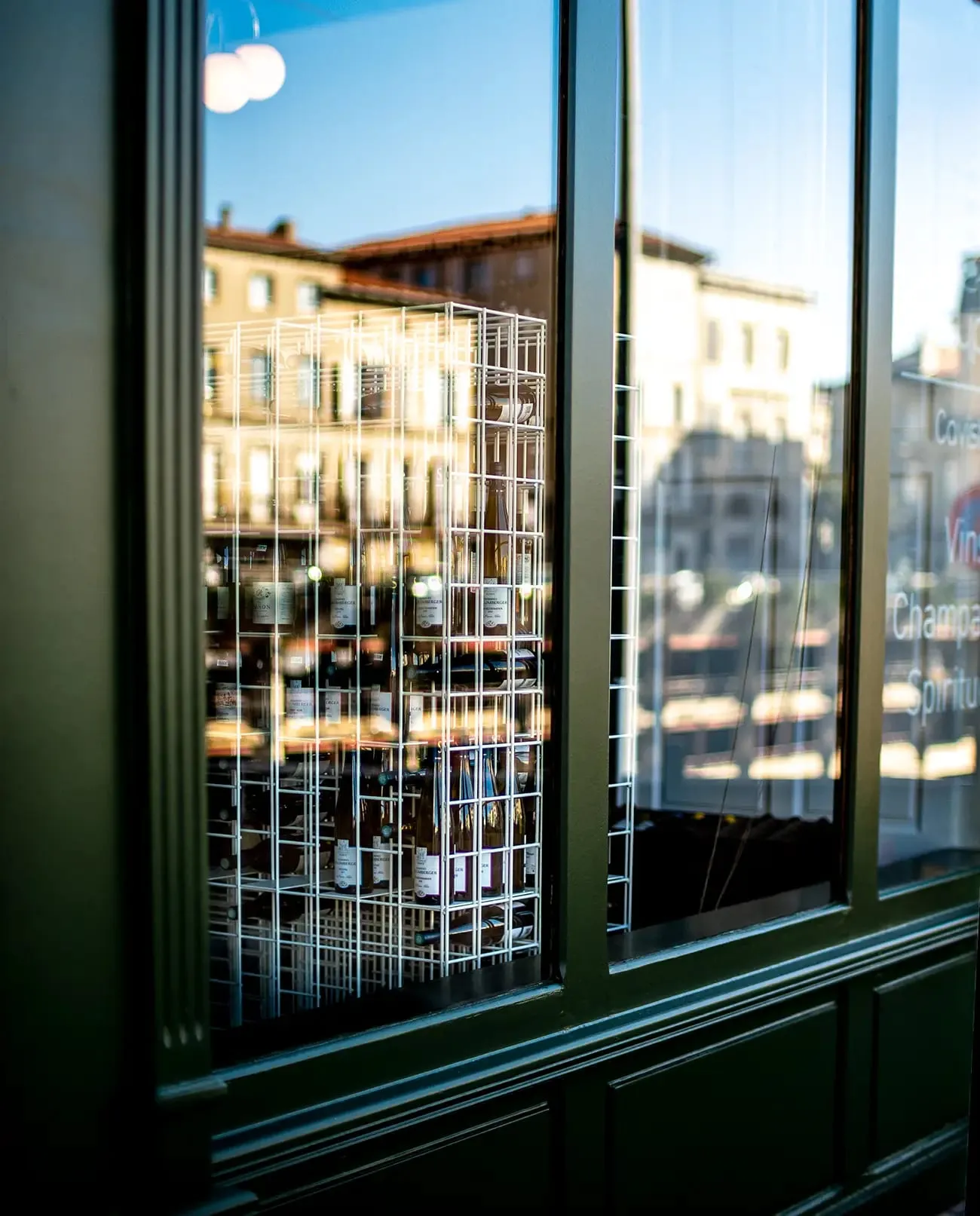 Reflets de la place de Castres dans la vitrine de L'Atypique, casiers à vin en fil d'acier
