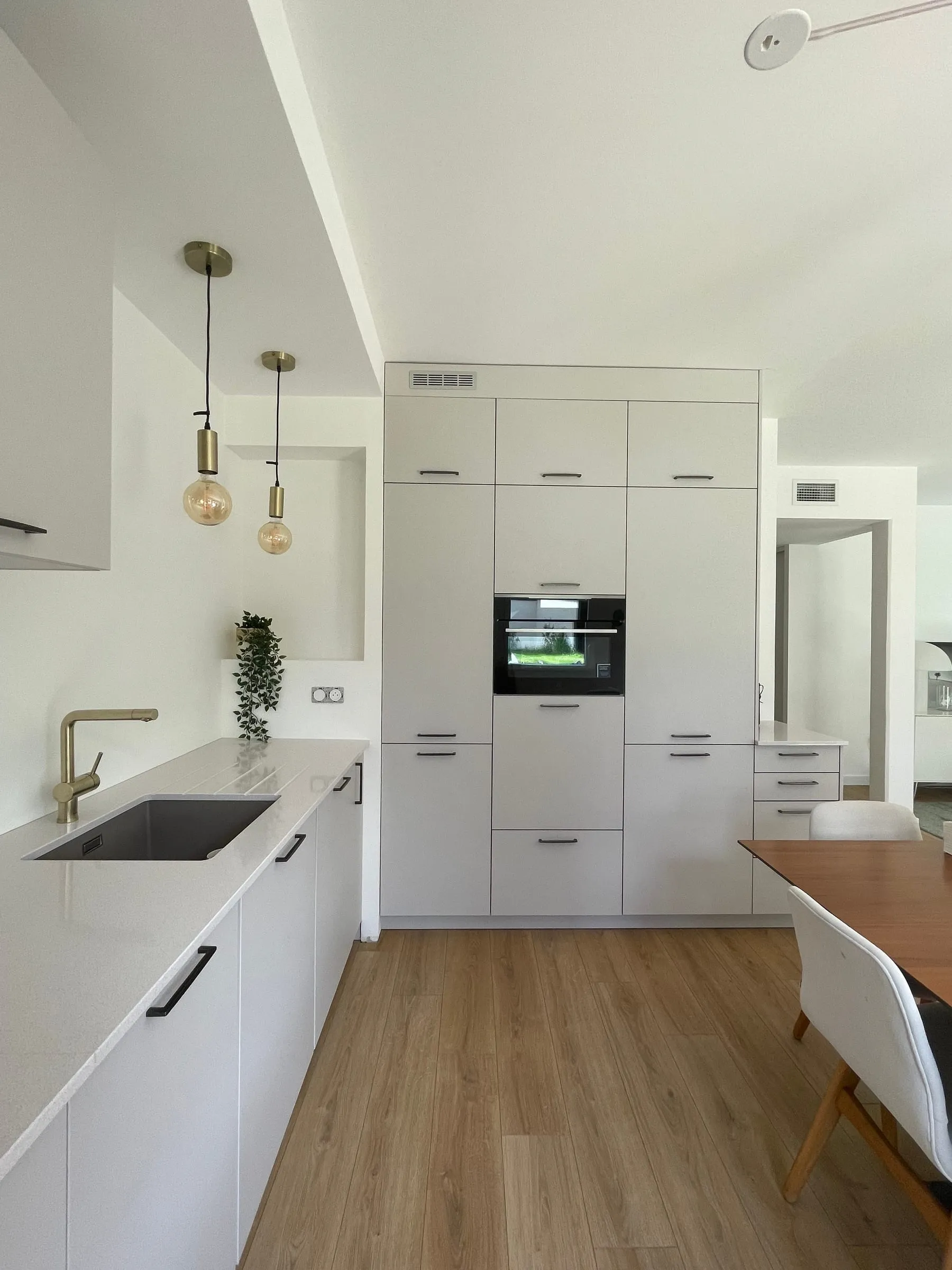 Cuisine blanche vue depuis l'entrée, suspensions en laiton et table à manger, Cuisine E1