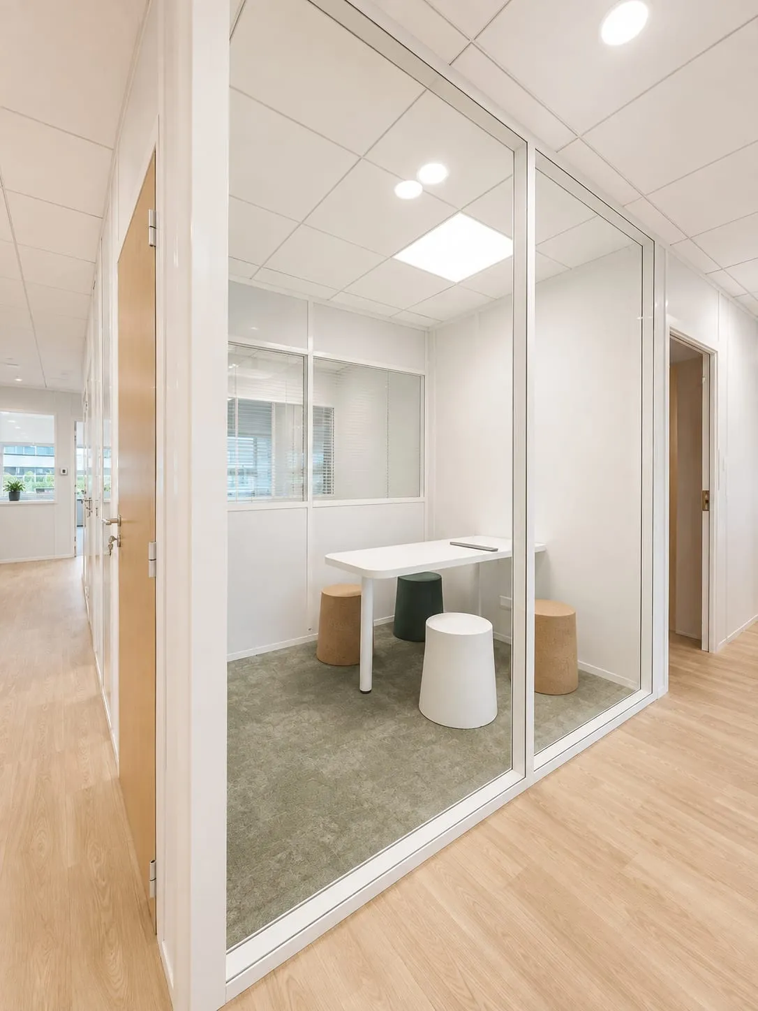 Bulle de réunion vitrée avec table blanche et tabourets, sol bois et moquette verte, CMCAS