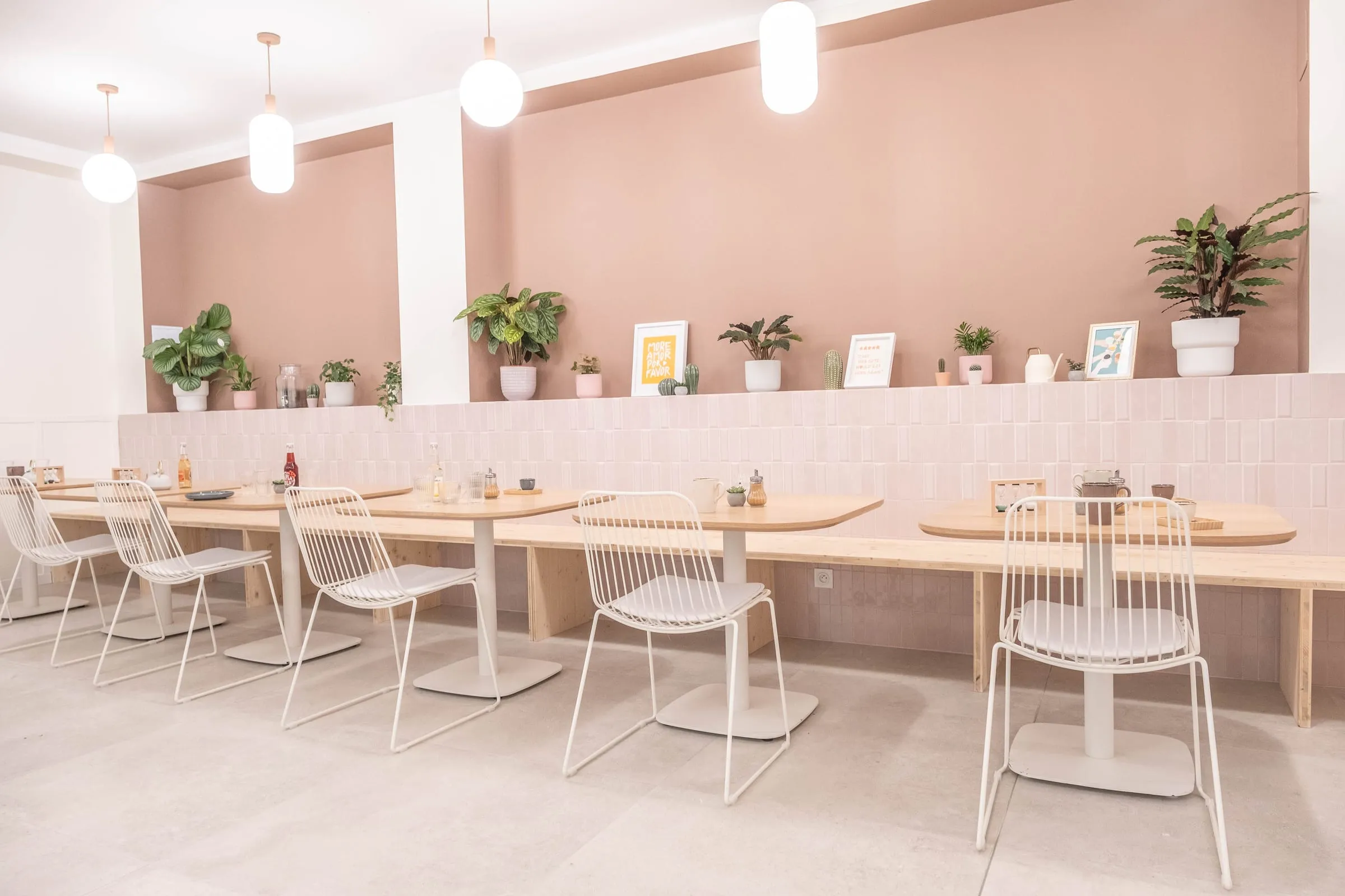 Enfilade de tables en bois et chaises blanches le long du mur terracotta, Kimi Coffee