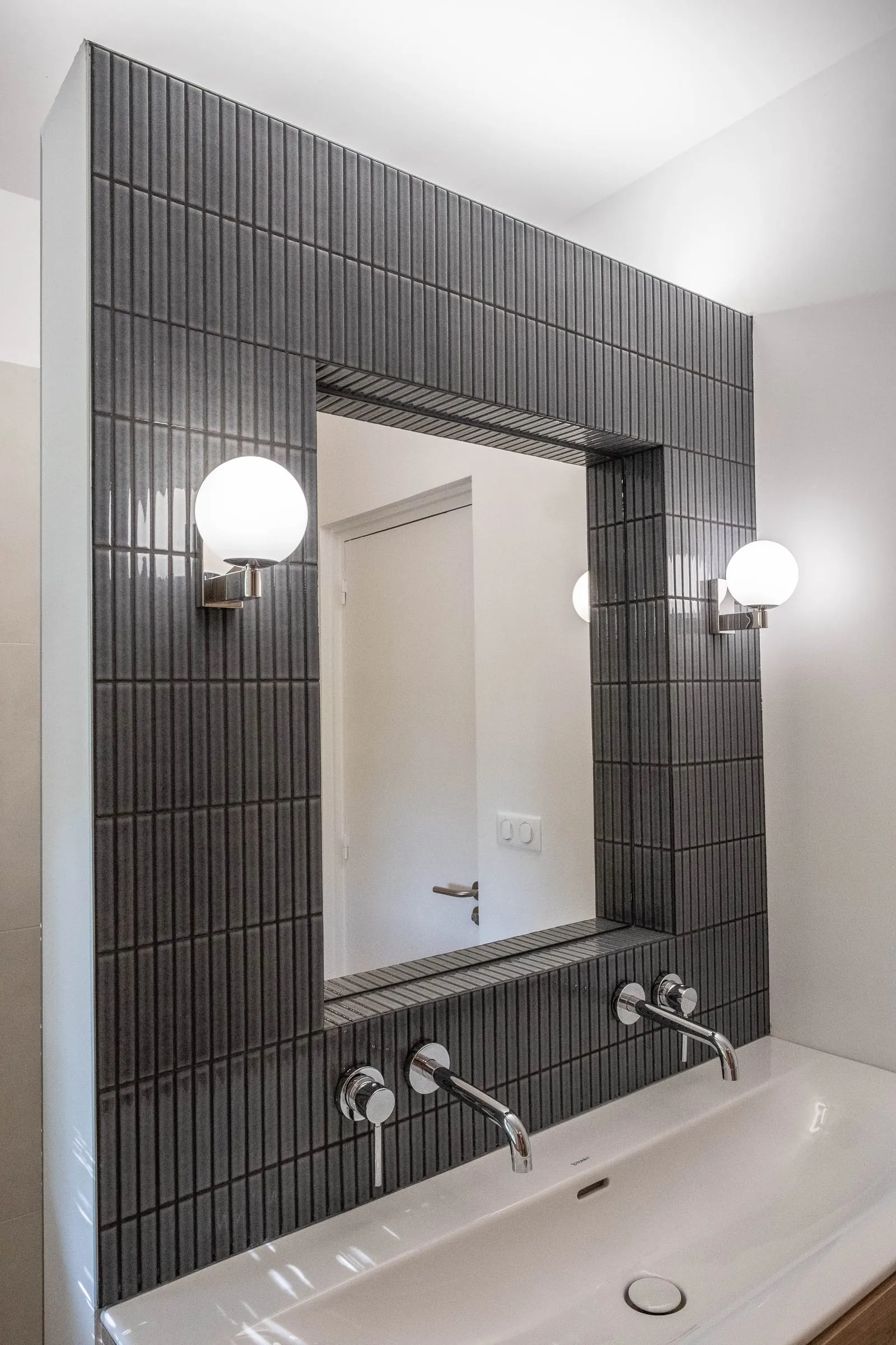 Miroir encadré de carrelage strié noir, deux appliques globe, D1
