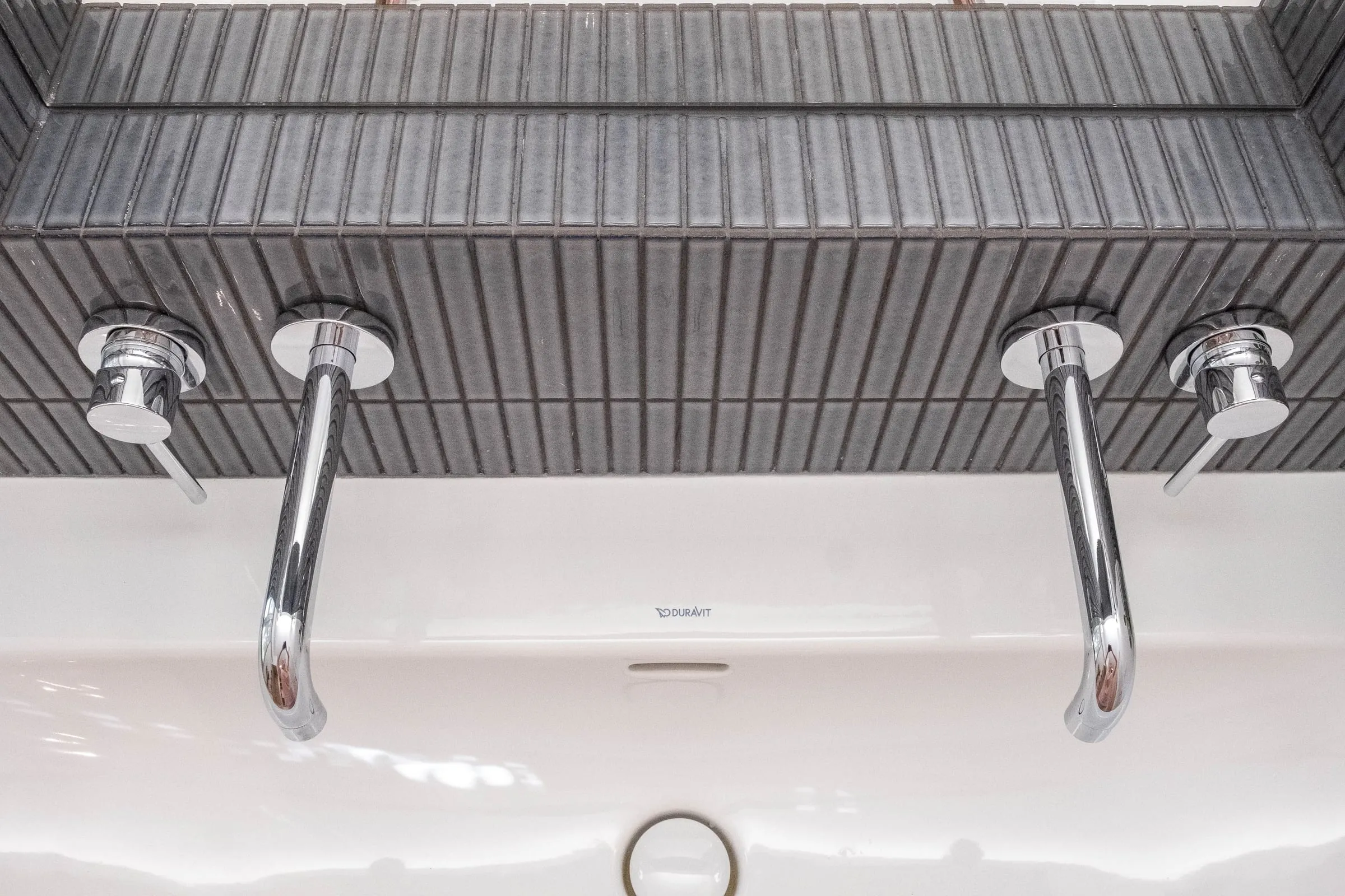 Deux robinets muraux chromés au-dessus de la baignoire, carrelage strié noir, D1